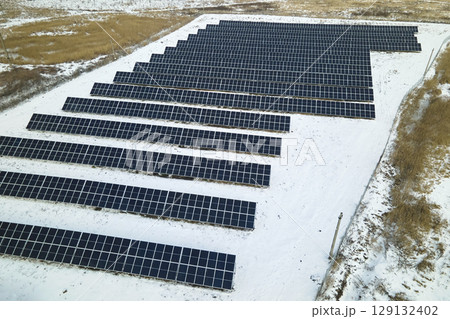 Aerial view of electrical power plant with solar panels covered with snow melting down in winter end for producing clean energy. Concept of low effectivity of renewable electricity in northern region 129132402