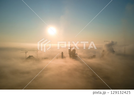 Aerial view of cement factory with high concrete plant structure and tower crane at industrial production site on foggy morning. Manufacture and global industry concept. Aerial view of cement factory with high concrete plant structure and tower crane at industrial production site on foggy morning. Manufacture and global industry concept. 129132425