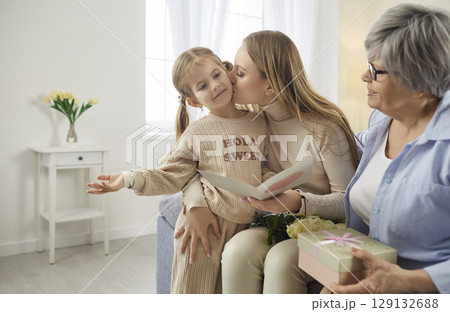 Child girl congratulating mother and grandmother on holiday sitting on sofa at home. Child girl congratulating mother and grandmother on holiday sitting on sofa at home. 129132688