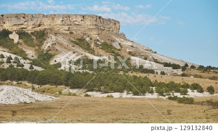 White rocky mountain rising through verdant forest, green slopes contrasting against vivid azure sky White rocky mountain rising through verdant forest, green slopes contrasting against vivid azure sky 129132840