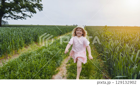Cheerful young woman running barefoot through golden wheat field, straw hat blowing, enjoying golden hour sunlight Cheerful young woman running barefoot through golden wheat field, straw hat blowing, enjoying golden hour sunlight 129132902