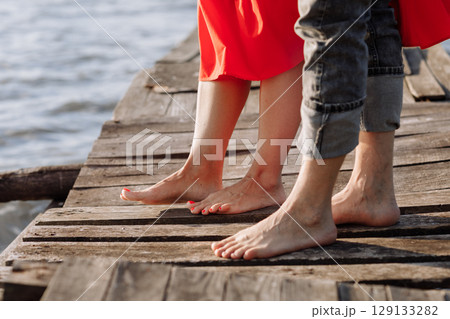 Cropped photo young lovers married couple, husband and wife, held of hands on a wooden bridge near lake. Rear view of couple standing on pier. lower half. Place for text and design. Close Up. Cropped photo young lovers married couple, husband and wife, held of hands on a wooden bridge near lake. Rear view of couple standing on pier. lower half. Place for text and design. Close Up. 129133282