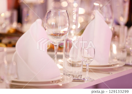 Empty glass set in restaurant. wedding, decor, celebration, holiday concept - romantic table setting with white tablecloth, plates, crystal glasses Empty glass set in restaurant. wedding, decor, celebration, holiday concept - romantic table setting with white tablecloth, plates, crystal glasses 129133299