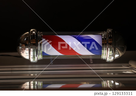 Barber pole spinning at night. International barbershop pole sign. A barber pole calling for people at street. Vintage barbershop. Salon. 129133311