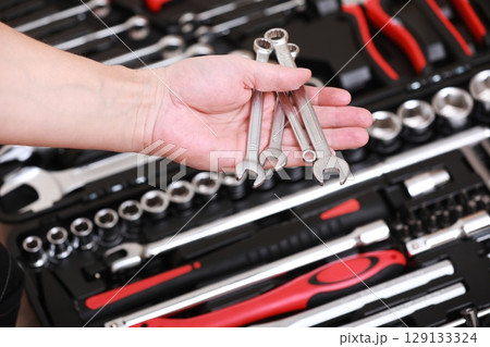 Tool store. Closeup of male hand holding wrenches. Auto repair kit in toolbox. Repairman instruments set. Inside the toolbox there are black-red wrenches, spanners and different nozzles. Closeup. 129133324