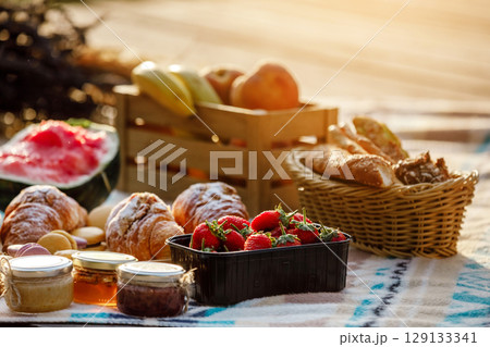 summer picnic basket with fruit and bakery on a blanket outdoors. Lunch with croissants, jam, watermelon, strawberry and fresh fruits in wooden box in the park. Copy space. 129133341