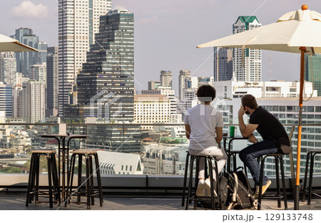Two men tourists while relaxing looking at Modern skyscrapers of Bangkok city. 129133748