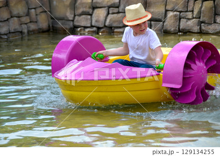 Kid playing rowing water paddle boat. Soft focus. A little girl rides a colorful boat on a pool in a resort. High quality photo 129134255