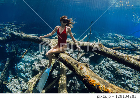 Freediver woman sitting on sunken log in crystal water. Freediving in fresh water lake in Indonesia 129134283