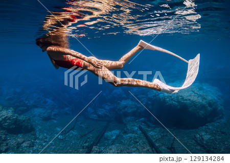Freediver woman with diving fins swims in transparent lake in sunny day 129134284