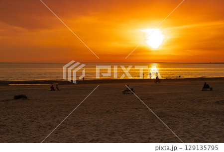 Summer evening at the beach. People watching the sunset over the sea. The sun sets on the water. The sky is painted with golden bright colors. Nature background. 129135795