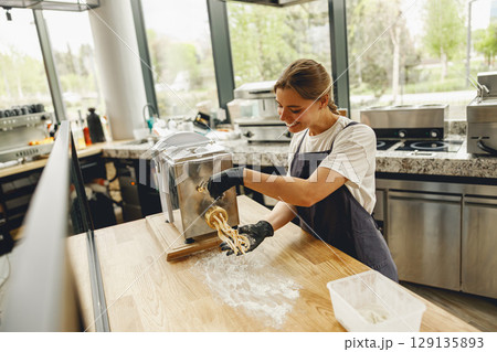 A Young Woman Engaged in the Art of Making Fresh Pasta in a Modern Equipped Kitchen A Young Woman Engaged in the Art of Making Fresh Pasta in a Modern Equipped Kitchen 129135893