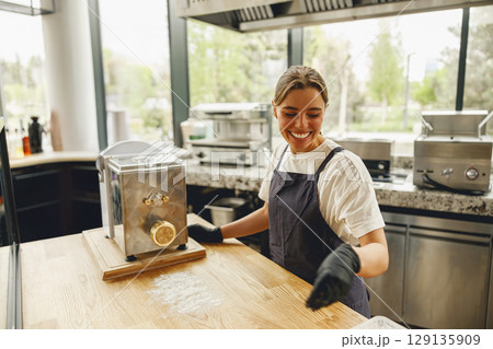 A Cheerful Baker Smiling in a Modern Kitchen While Using a Pasta Maker for Culinary Art 129135909