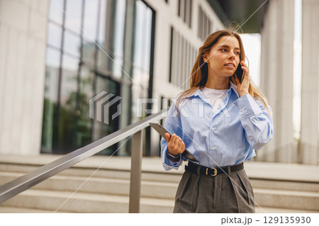 A young woman in a stylish blue shirt is using her smartphone outside a modern building A young woman in a stylish blue shirt is using her smartphone outside a modern building 129135930