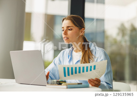 A Focused Professional Dedicatedly Analyzing Data on a Laptop at a Modern, Trendy Workspace 129135965