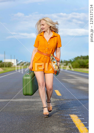 Blonde woman with a green retro suitcase walking on the highway. Blonde woman with a green retro suitcase walking on the highway. 129137134