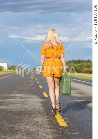 Blonde woman with a green retro suitcase walking on the highway. Blonde woman with a green retro suitcase walking on the highway. 129137136