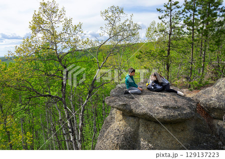 Two teen hikers are sitting on top of rock structures. Two teen hikers are sitting on top of rock structures. 129137223