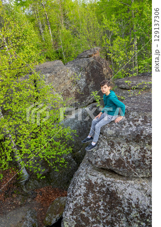 Boy is sitting on big Rocks formation in the green forest. 129137306