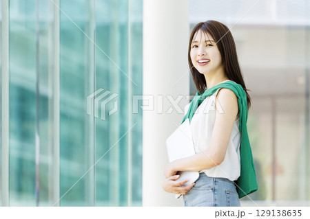 大学の廊下でノートパソコンを持つ笑顔の女子大生 129138635