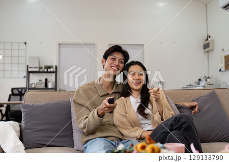 Happy Couple Relaxing on Sofa Watching TV in Modern Living Room with Cozy Decor and Warm Lighting 129138790