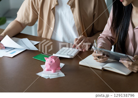 Couple Calculating Finances with Piggy Bank and Digital Devices for Effective Money Saving and Budget Planning at Home Couple Calculating Finances with Piggy Bank and Digital Devices for Effective Money Saving and Budget Planning at Home 129138796