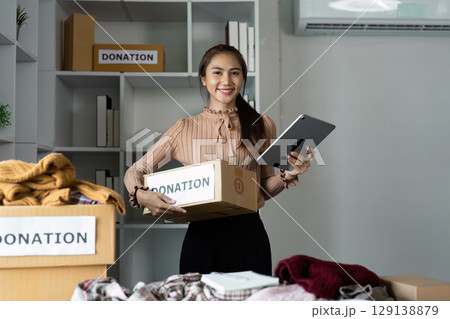 Smiling Woman Organizing Donations with Tablet in Modern Office Setting 129138879