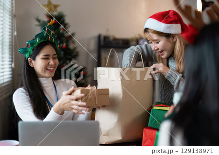 Joyful Christmas Celebration with Friends Exchanging Gifts by the Christmas Tree in a Cozy Living Room Setting 129138971