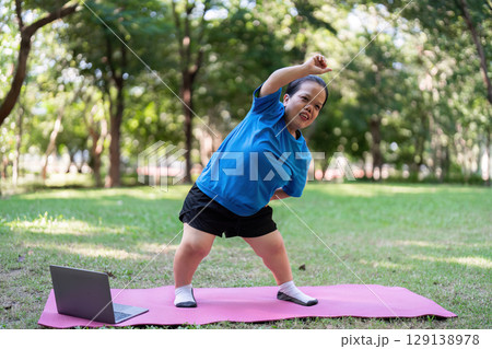Woman Exercising Outdoors on Yoga Mat with Laptop in Park Setting for Fitness and Wellness Inspiration 129138978