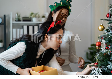 Festive Holiday Scene with Women Decorating Christmas Tree in Cozy Home Setting with Ornaments and Seasonal Decorations Festive Holiday Scene with Women Decorating Christmas Tree in Cozy Home Setting with Ornaments and Seasonal Decorations 129139032