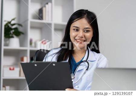 Confident Female Doctor in White Coat with Stethoscope Reviewing Patient Chart in Modern Medical Office 129139107
