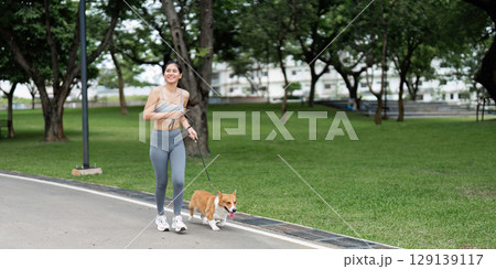 Joyful Woman Running with Corgi in Urban Park Joyful Woman Running with Corgi in Urban Park 129139117