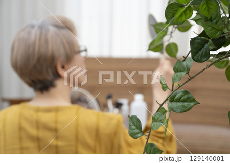 リビングで手鏡で後頭部を見る高齢者 シニア女性のヘアケア ボケ リビングで手鏡で後頭部を見る高齢者 シニア女性のヘアケア ボケ 129140001
