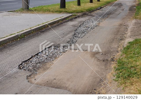 The road surface in this area has significant damage, featuring numerous potholes and repairs 129140029