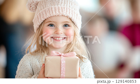 joyful girl holding gift during Christmas celebrations with family gathering together. festive holiday seasonal Christmas New Year atmosphere is enhanced by decorated tree and smiling faces 129140853
