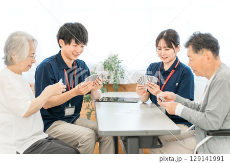 グループホーム,老人ホームでトランプをする高齢者と介護士の男女スタッフ 129141991