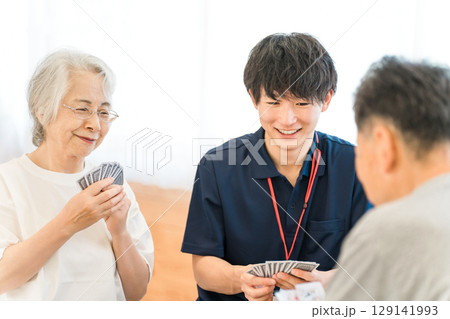 グループホーム,老人ホームでトランプをする高齢者と介護士の男性スタッフ 129141993
