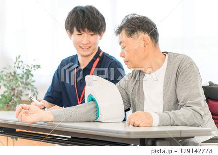 血圧計を使い血圧測定をするシニア男性と記録をとる看護師,介護士の男性スタッフ 血圧計を使い血圧測定をするシニア男性と記録をとる看護師,介護士の男性スタッフ 129142728