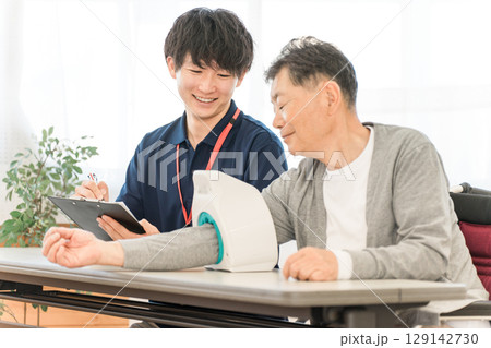 血圧計を使い血圧測定をするシニア男性と記録をとる看護師,介護士の男性スタッフ 血圧計を使い血圧測定をするシニア男性と記録をとる看護師,介護士の男性スタッフ 129142730