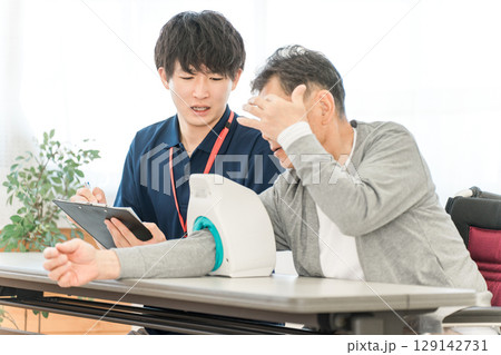 血圧計を使い血圧測定をするシニア男性と記録をとる看護師,介護士の男性スタッフ 血圧計を使い血圧測定をするシニア男性と記録をとる看護師,介護士の男性スタッフ 129142731