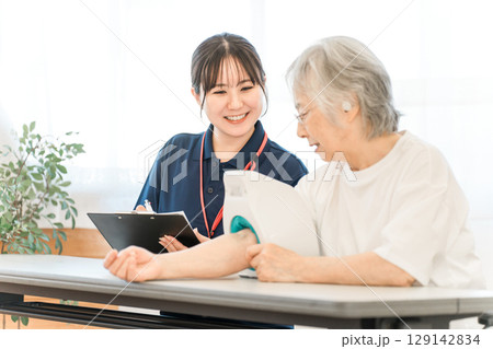 血圧計を使い血圧測定をするシニア女性と記録をとる看護師,介護士の女性スタッフ 129142834