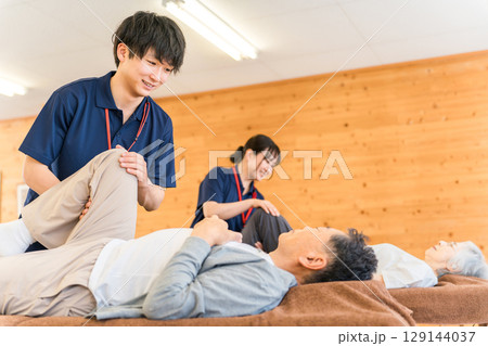 リハビリでマッサージ・ストレッチをするシニア男性と理学療法士・作業療法士の男性スタッフ 129144037