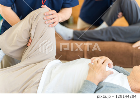 整形外科,病院の施術ベットで理学療法士から施術を受けるシニア男性 整形外科,病院の施術ベットで理学療法士から施術を受けるシニア男性 129144284