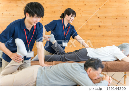リハビリでマッサージ・ストレッチをするシニア男性と理学療法士・作業療法士の男性スタッフ リハビリでマッサージ・ストレッチをするシニア男性と理学療法士・作業療法士の男性スタッフ 129144290