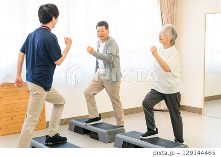 デイサービス・パーソナルジムでトレーニングするシニア世代の男女とインストラクターの若い男性 129144465