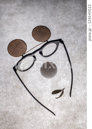 Sunglasses with double glass, a white ball and a leaf in the shape of a face on a gray background 129145015