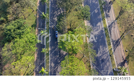 An aerial view of a wide, multi-lane road flanked by trees, with cars and motorbikes driving on a sunny day. An aerial view of a wide, multi-lane road flanked by trees, with cars and motorbikes driving on a sunny day. 129145955