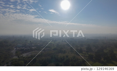 A hazy, sun-drenched aerial view of a sprawling landscape, with a mix of fields, trees, and scattered buildings under a bright sky with wispy clouds. A hazy, sun-drenched aerial view of a sprawling landscape, with a mix of fields, trees, and scattered buildings under a bright sky with wispy clouds. 129146169