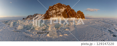 Beautiful winter landscape of frozen Lake Baikal at sunrise - A granite rock with steep slopes rises above a frozen lake - Baikal lake, Siberia. Winter ice covers providing a stunning backdrop for Beautiful winter landscape of frozen Lake Baikal at sunrise - A granite rock with steep slopes rises above a frozen lake - Baikal lake, Siberia. Winter ice covers providing a stunning backdrop for 129147220