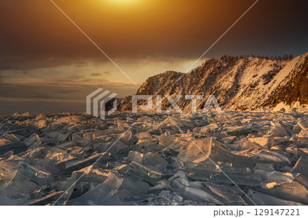 Beautiful winter landscape of frozen Lake Baikal at sunrise - A granite rock with steep slopes rises above a frozen lake. Winter ice covers providing a stunning backdrop for winter tourism adventures. Beautiful winter landscape of frozen Lake Baikal at sunrise - A granite rock with steep slopes rises above a frozen lake. Winter ice covers providing a stunning backdrop for winter tourism adventures. 129147221